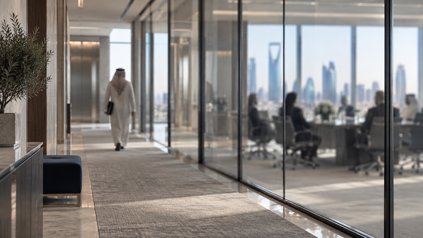 A corridor outside a glass-walled boardroom in Riyadh; the board sits behind the glass, out of focus, while one figure seen from behind walks away toward the lifts with a folder under his arm.